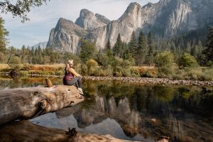 Image of woman sitting on a fallen tree log while overlooking big mountains in Yosemite