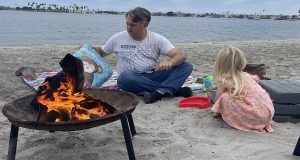 A man and child play in the sand near a bonfire