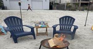 Two chairs and a table with smores ingredients are set up near a bonfire